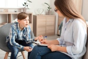 a teen boy talks to a therapist about adolescent mental health treatment 
