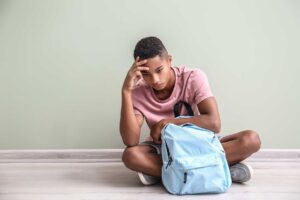 Teen with co-occurring disorders sitting on the floor with his backpack struggling with dual diagnosis symptoms