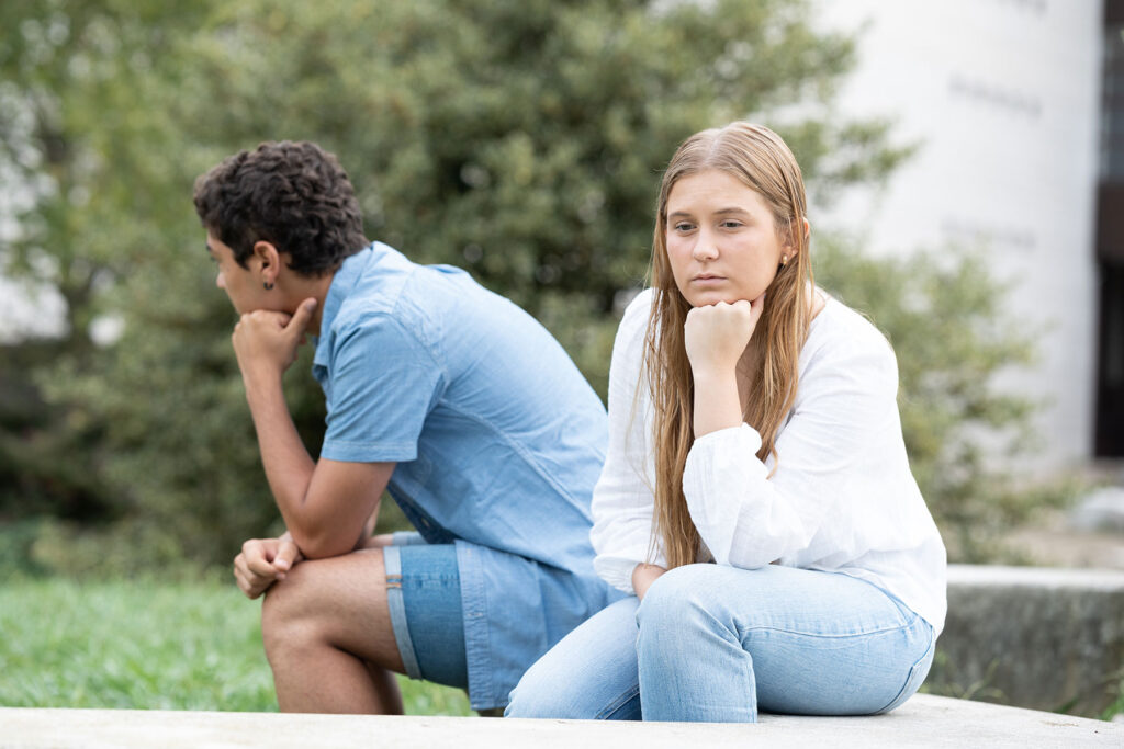 Young couple sitting on park bench facing away from each other while dealing with red flags in teenage relationships