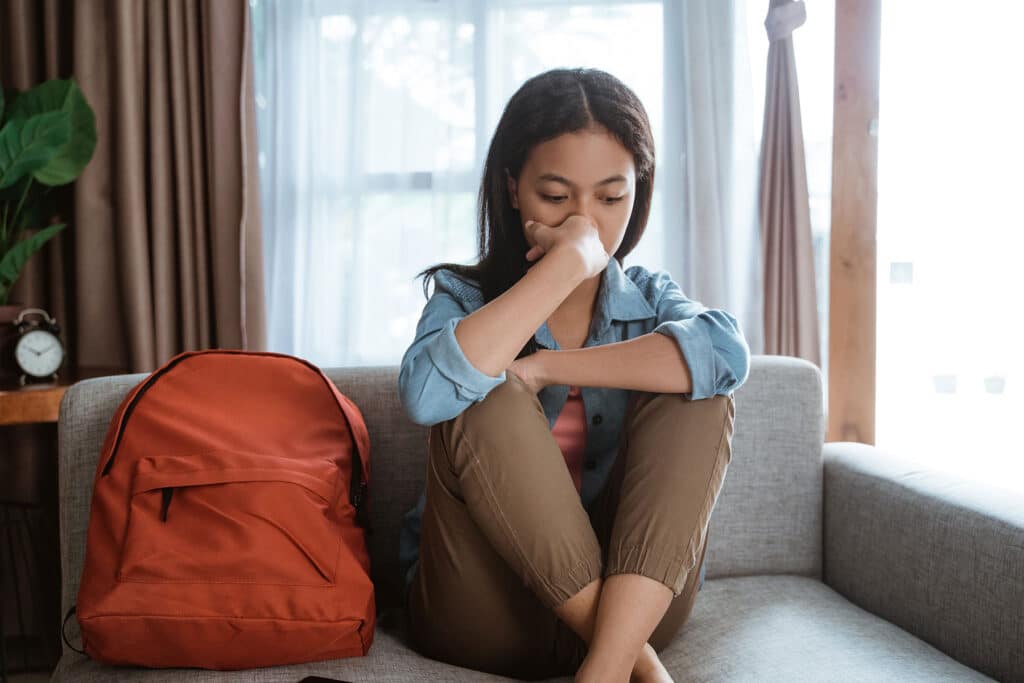 Teen sitting on couch experiencing depression as one of the long term effects of losing a parent