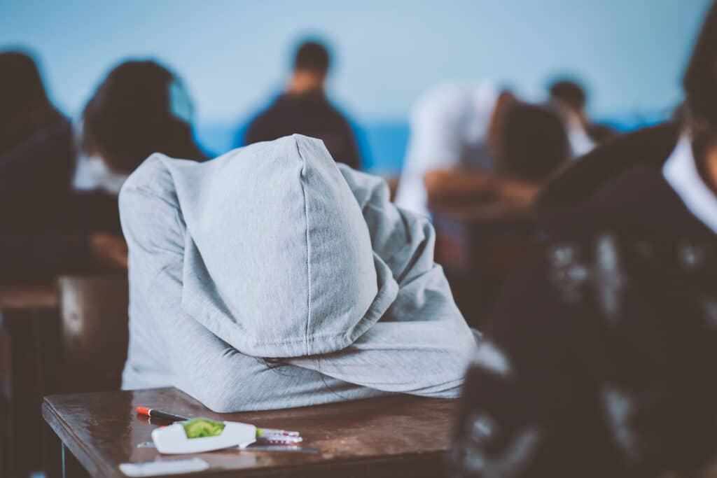 teen in hoodie with head down against desk in classroom as one example of how to identify depression in teens